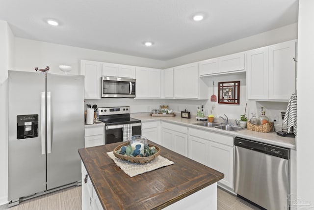 kitchen with butcher block counters, a kitchen island, stainless steel appliances, white cabinetry, and a sink