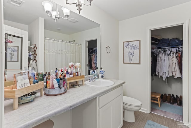 bathroom featuring a chandelier, toilet, vanity, visible vents, and a walk in closet