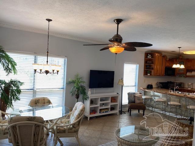 tiled living room with ceiling fan with notable chandelier, ornamental molding, and a textured ceiling