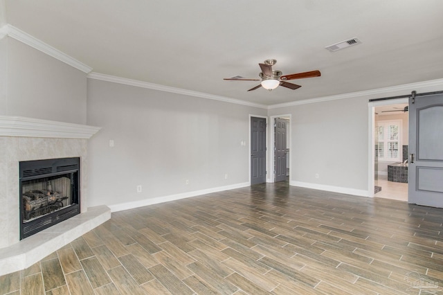 unfurnished living room with crown molding, a barn door, and ceiling fan