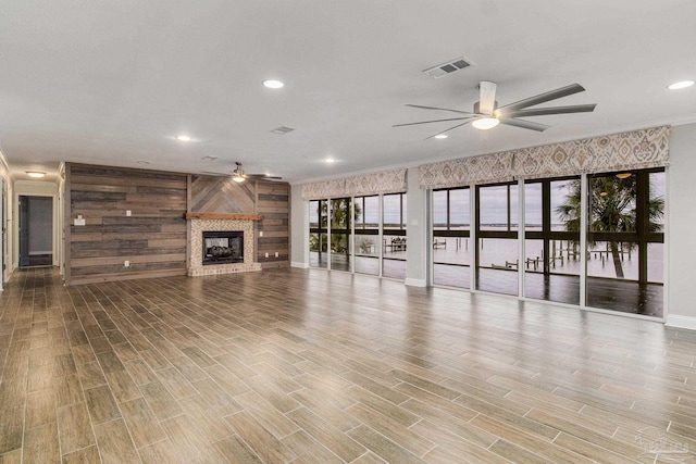 unfurnished living room with ornamental molding, wooden walls, and ceiling fan