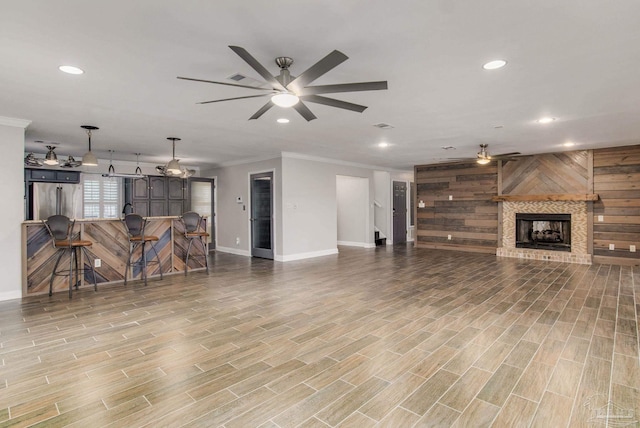 living room featuring ceiling fan, wooden walls, ornamental molding, bar area, and a brick fireplace