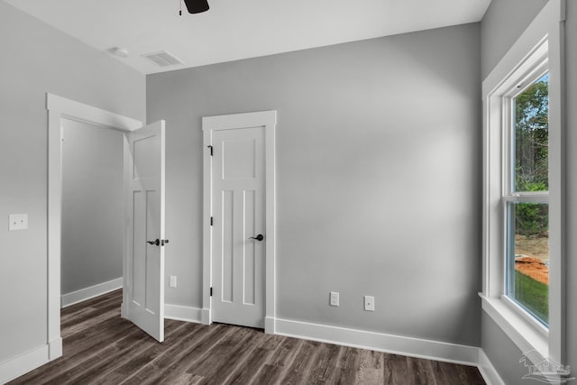 unfurnished bedroom featuring multiple windows, dark wood-style floors, visible vents, and baseboards