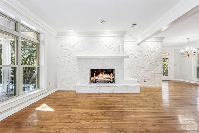 unfurnished living room featuring crown molding, a notable chandelier, a stone fireplace, and hardwood / wood-style flooring