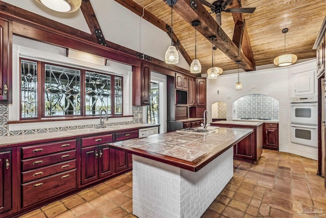 kitchen featuring sink, wooden ceiling, white double oven, an island with sink, and beamed ceiling