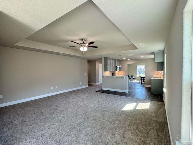 unfurnished living room with ceiling fan, a raised ceiling, and dark colored carpet