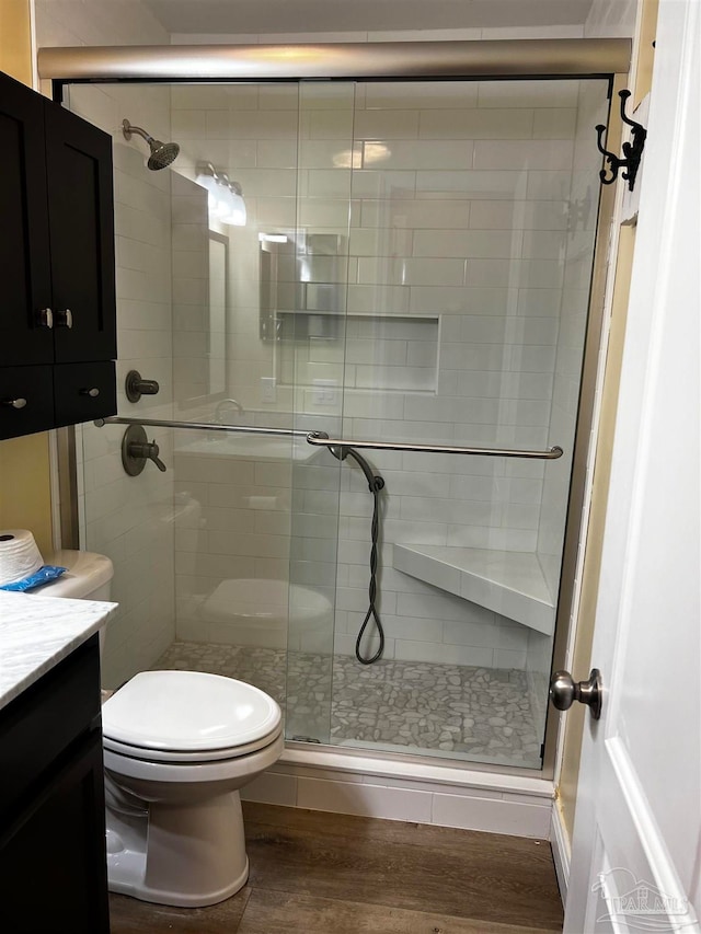 bathroom with hardwood / wood-style floors, vanity, toilet, and a shower with shower door