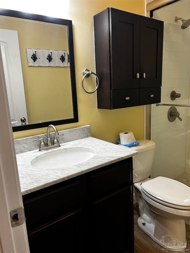 bathroom featuring a tile shower, vanity, wood-type flooring, and toilet