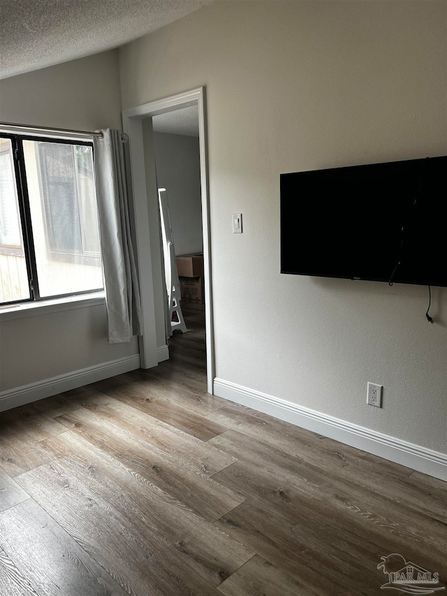 empty room featuring a textured ceiling, light hardwood / wood-style floors, and lofted ceiling