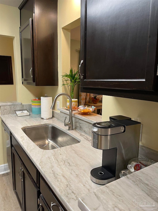 kitchen with sink, light stone counters, light hardwood / wood-style flooring, stainless steel dishwasher, and dark brown cabinets