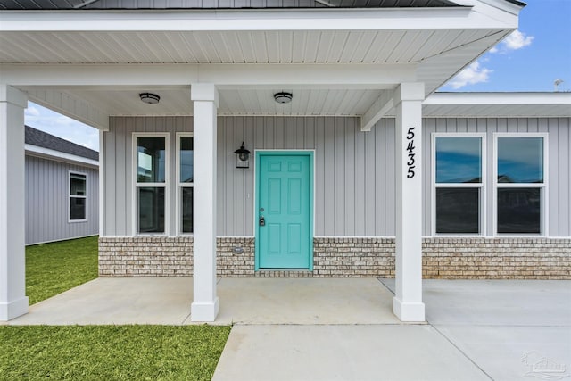 doorway to property with brick siding, board and batten siding, and a porch