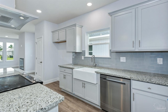 kitchen with wood finished floors, light stone countertops, a sink, decorative backsplash, and stainless steel dishwasher