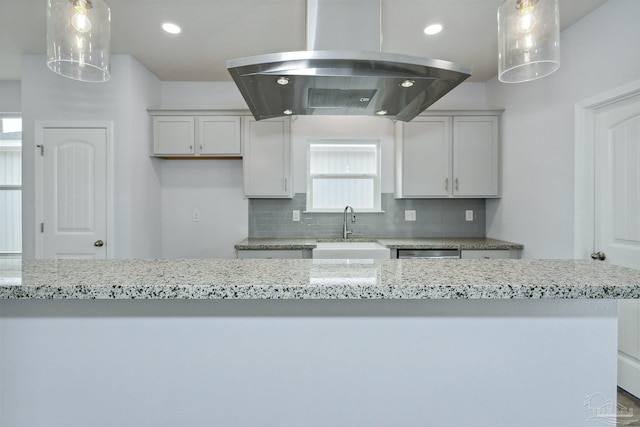 kitchen with light stone counters, island exhaust hood, a sink, decorative backsplash, and stainless steel dishwasher