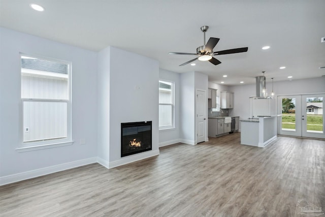 unfurnished living room with baseboards, recessed lighting, french doors, a glass covered fireplace, and light wood-type flooring