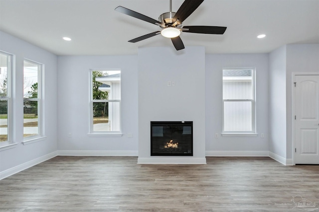 unfurnished living room with recessed lighting, baseboards, a glass covered fireplace, and wood finished floors