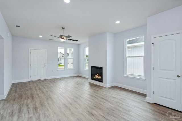 unfurnished living room with wood finished floors, visible vents, baseboards, recessed lighting, and a glass covered fireplace