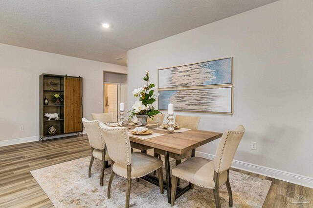 dining room featuring a barn door, hardwood / wood-style flooring, and a textured ceiling