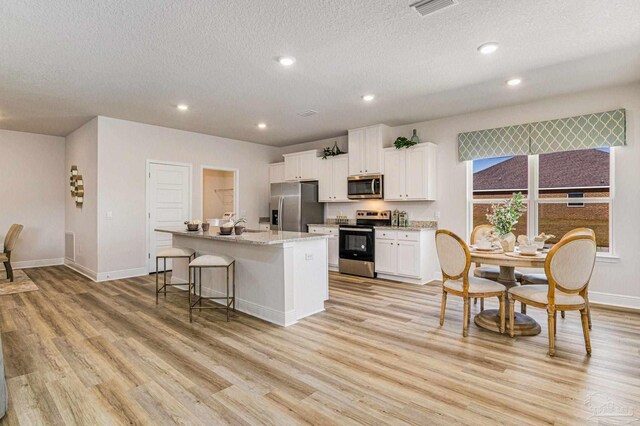 kitchen featuring light hardwood / wood-style floors, an island with sink, a kitchen breakfast bar, white cabinetry, and appliances with stainless steel finishes