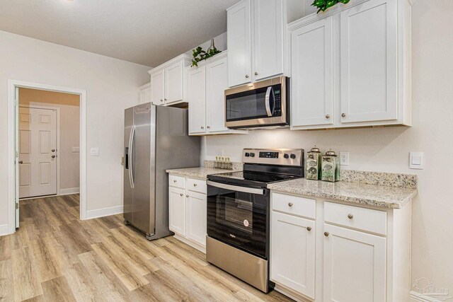 kitchen featuring white cabinetry, light stone countertops, appliances with stainless steel finishes, and light hardwood / wood-style flooring