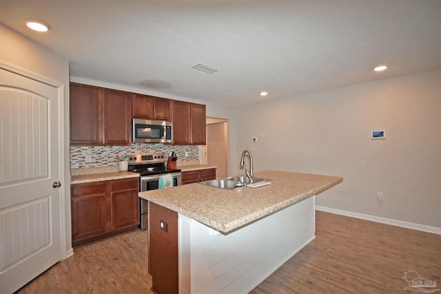 9453 Lutoo Ln, Pensacola, FL 32526 - kitchen with stainless steel appliances, a sink, light wood-style flooring, backsplash, and a kitchen island with sink