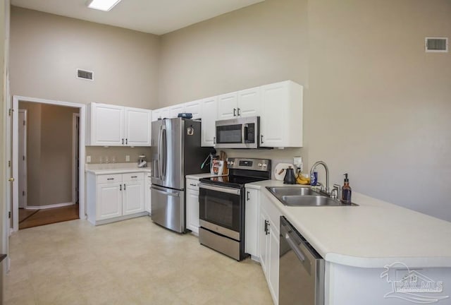 kitchen featuring appliances with stainless steel finishes, light tile patterned floors, sink, a high ceiling, and kitchen peninsula