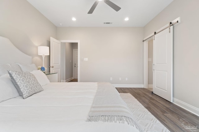 bedroom with ceiling fan, a barn door, and dark hardwood / wood-style flooring