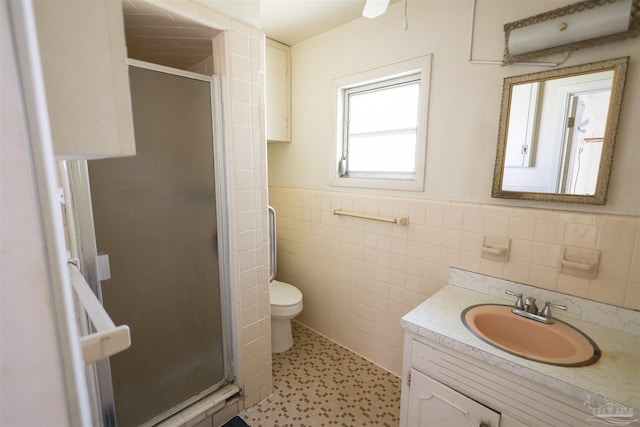 bathroom featuring a shower with door, vanity, tile walls, and toilet