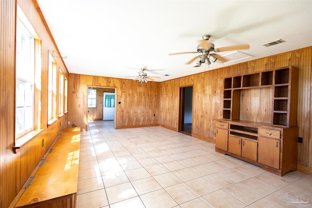 unfurnished living room with wood walls, light tile patterned floors, and ceiling fan