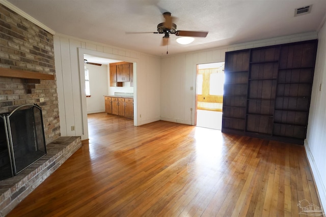 unfurnished living room featuring ceiling fan, ornamental molding, light hardwood / wood-style floors, and a brick fireplace