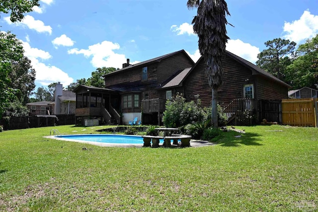 back of property with a fenced in pool, a sunroom, and a lawn