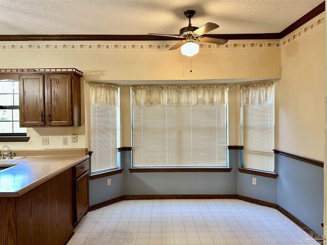 kitchen featuring dark brown cabinetry, crown molding, ceiling fan, and a textured ceiling