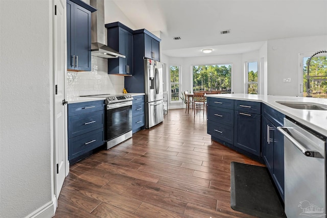 kitchen featuring wall chimney range hood, sink, decorative backsplash, blue cabinetry, and stainless steel appliances