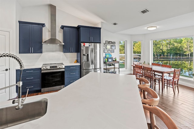 kitchen with tasteful backsplash, stainless steel appliances, sink, blue cabinetry, and wall chimney range hood