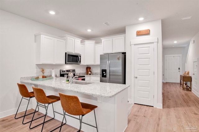 kitchen with light stone countertops, kitchen peninsula, light hardwood / wood-style floors, stainless steel appliances, and white cabinets