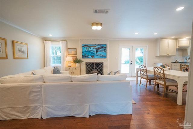 living room featuring a healthy amount of sunlight, dark hardwood / wood-style flooring, ornamental molding, and a brick fireplace