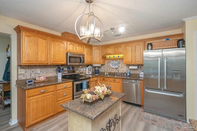 kitchen featuring a textured ceiling, pendant lighting, a kitchen island, an inviting chandelier, and appliances with stainless steel finishes