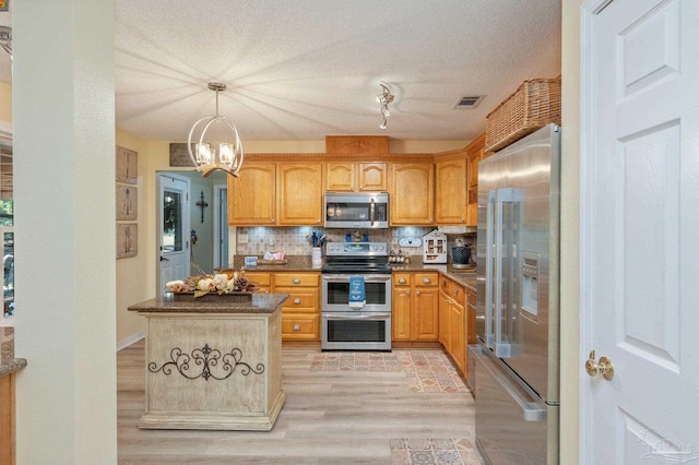 kitchen with appliances with stainless steel finishes, light hardwood / wood-style floors, a notable chandelier, pendant lighting, and backsplash