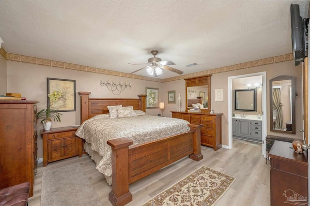 bedroom featuring a textured ceiling, connected bathroom, ceiling fan, and light wood-type flooring