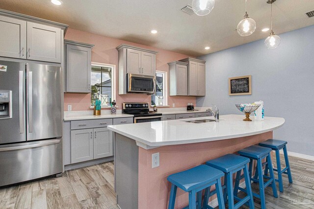 kitchen featuring stainless steel appliances, sink, gray cabinets, light hardwood / wood-style floors, and an island with sink