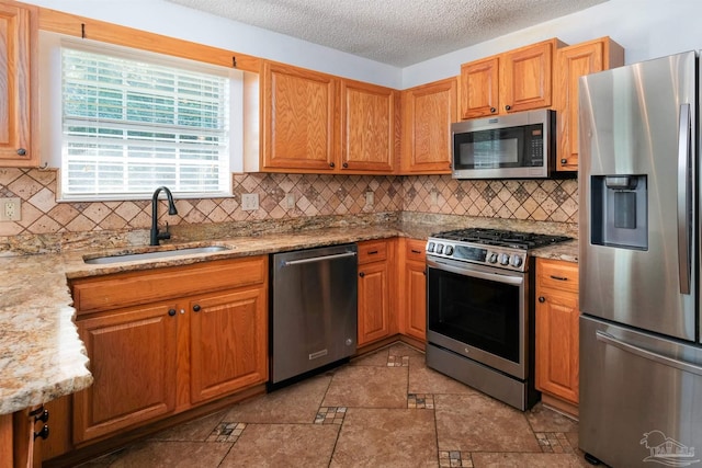 kitchen with appliances with stainless steel finishes, tasteful backsplash, light stone countertops, a textured ceiling, and sink