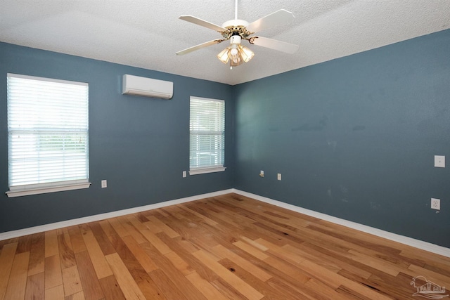 empty room with wood-type flooring, a textured ceiling, ceiling fan, and a wall mounted AC