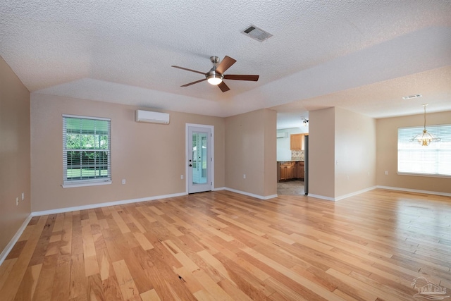 unfurnished room featuring a textured ceiling, light hardwood / wood-style flooring, a wall mounted air conditioner, and plenty of natural light