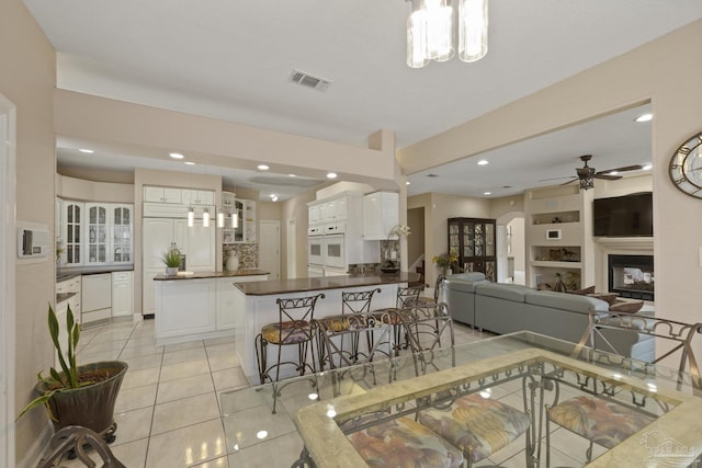 dining room featuring light tile patterned floors, arched walkways, recessed lighting, visible vents, and a glass covered fireplace