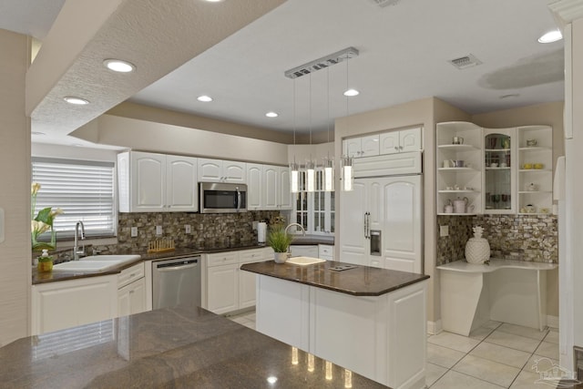 kitchen with a center island with sink, light tile patterned floors, stainless steel appliances, decorative backsplash, and white cabinets