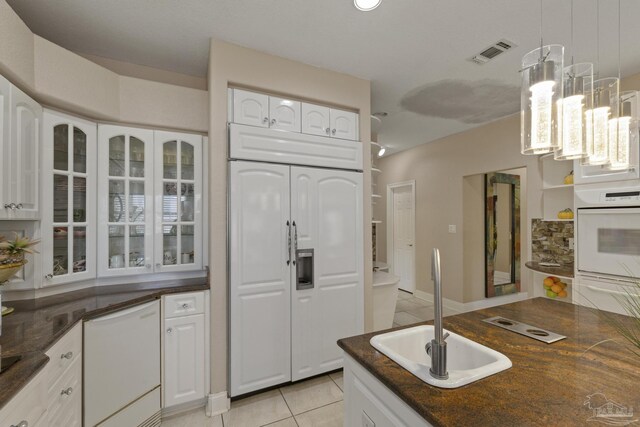 kitchen with light tile patterned flooring, white appliances, a sink, visible vents, and glass insert cabinets