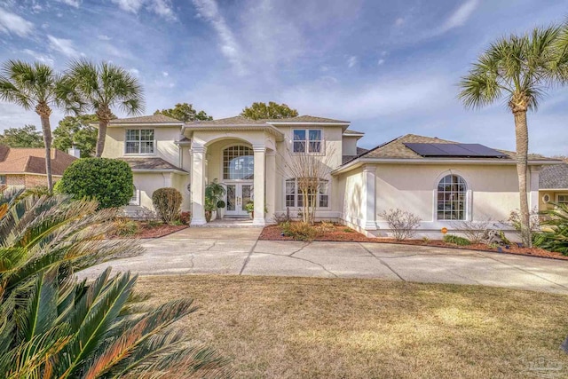 mediterranean / spanish house with roof mounted solar panels, a front lawn, french doors, and stucco siding