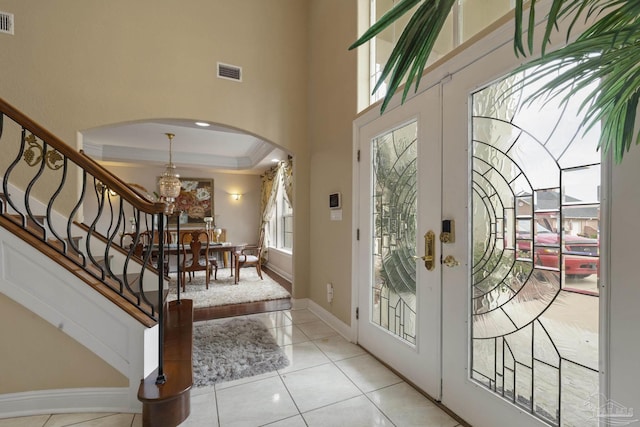 entryway with arched walkways, french doors, a raised ceiling, visible vents, and stairs