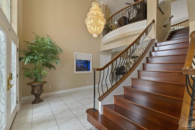 entrance foyer with a towering ceiling, baseboards, stairway, tile patterned floors, and an inviting chandelier