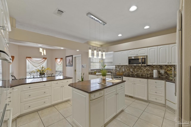 kitchen with light tile patterned floors, visible vents, dark countertops, stainless steel microwave, and a sink