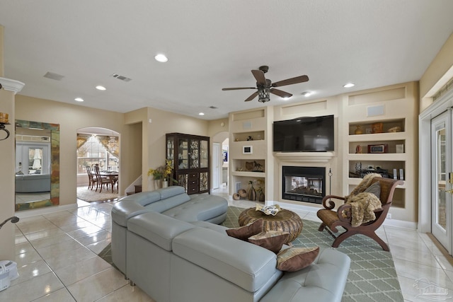 living area featuring light tile patterned floors, a glass covered fireplace, visible vents, and built in features